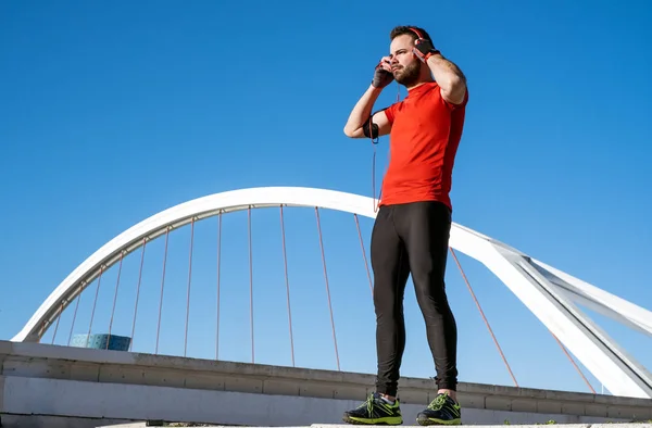 Young man preparing to run with a pair of headphones in front of a bridge — Stock Photo, Image