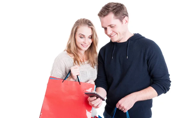 Casal segurando sacos de compras verificando smartphone — Fotografia de Stock