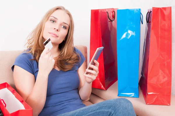 Lady sitting on couch thinking with smartphone and card — Stock Photo, Image