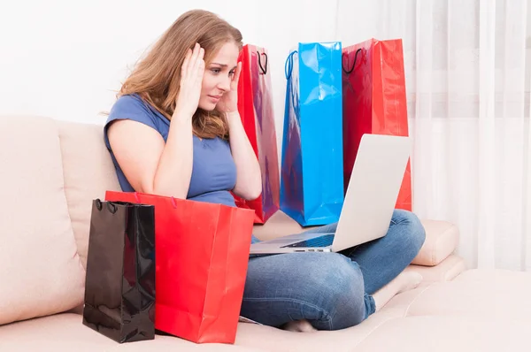 Shopaholic sitting on couch holding her head — Stock Photo, Image