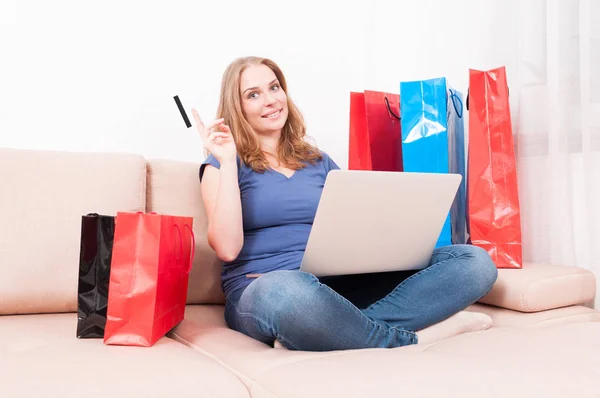 Mujer sentada en el sofá sosteniendo el ordenador portátil mostrando la tarjeta —  Fotos de Stock