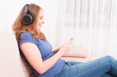 Akıllı telefon tutarak kulaklık dinleme kanepede oturan Bayan