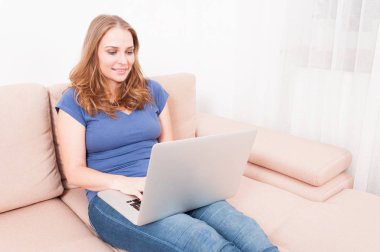 Gülümseyen ve koltukta oturan dizüstü bilgisayarda yazarak kadın