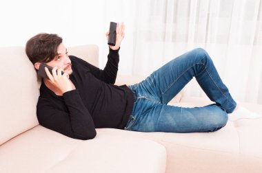 Adam akıllı telefon ve Uzaktan kumanda tutarak kanepenin üzerinde döşeme