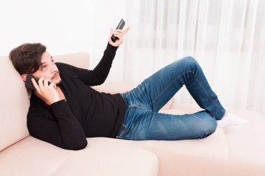 Adam akıllı telefon ve Uzaktan kumanda tutarak kanepenin üzerinde döşeme