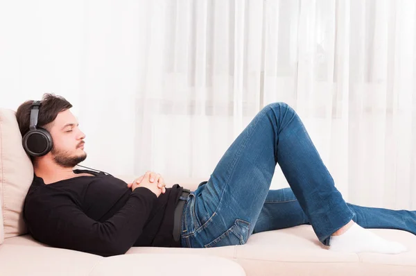 Man laying on sofa wearing headphones and relaxing