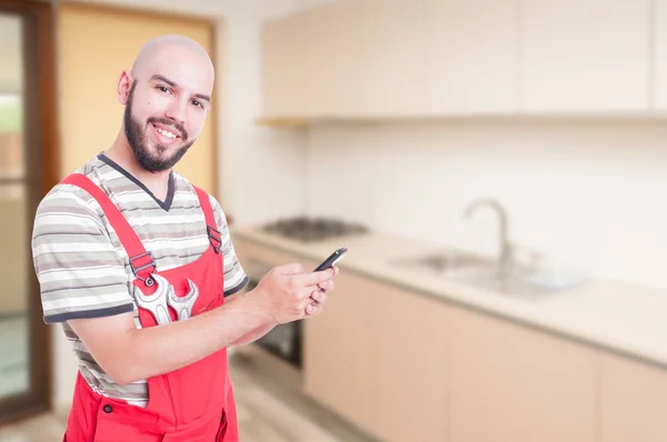 Vrolijke mannelijke loodgieter texting in de keuken — Stockfoto