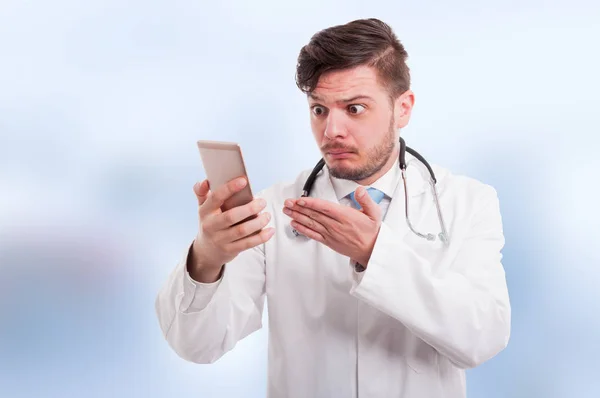 Un joven médico mirando perplejo a su teléfono — Foto de Stock