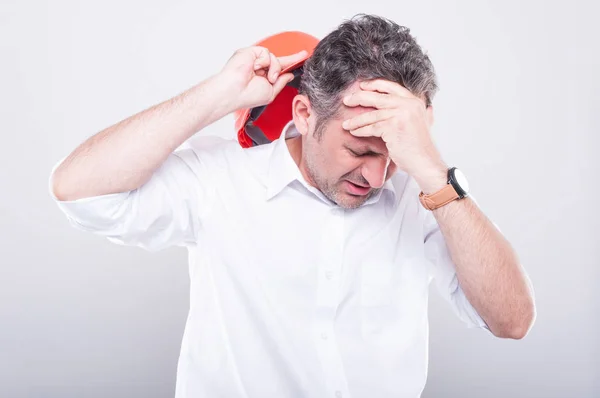 Retrato de empreiteiro usando chapéu duro fazendo gesto de dor de cabeça — Fotografia de Stock