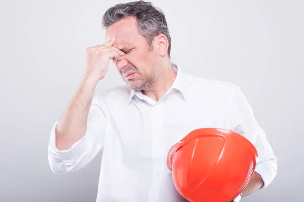 Portrait of architect holding hardhat making head ache gesture — Stock Photo, Image