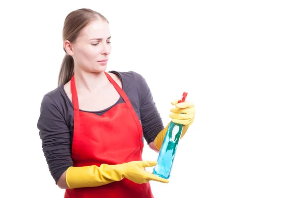 Bela empregada em roupas de trabalho olhando para spray de limpeza — Fotografia de Stock