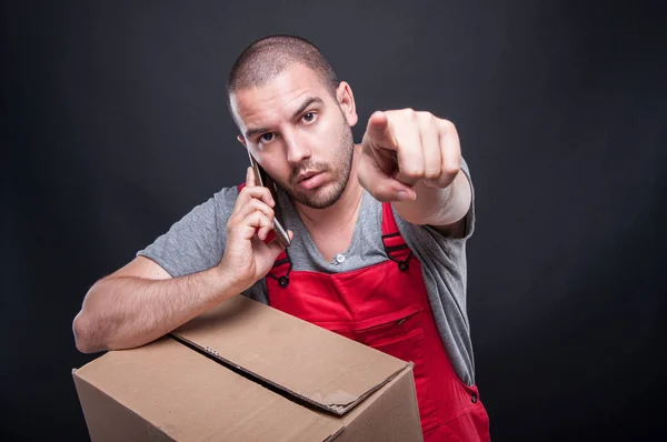 Mover man holding box talking at phone pointing camera — Stock Photo, Image