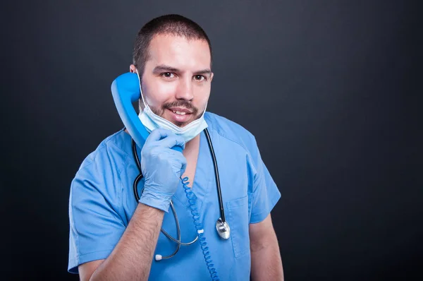 Doctor wearing scrubs holding telephone receiver and smiling — Stock Photo, Image