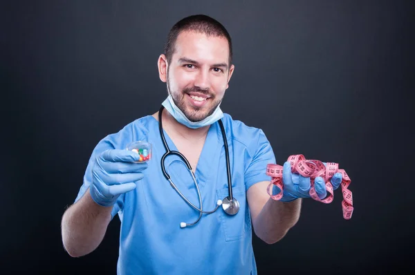 Plastic surgeon wearing scrubs holding measuring tape and pills — Stock Photo, Image