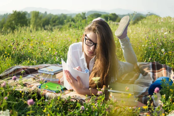 Gril liggande på gräset och skriva på anteckningsboken — Stockfoto