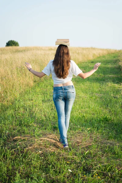 Caminhada feminina enquanto equilibra livros na cabeça — Fotografia de Stock