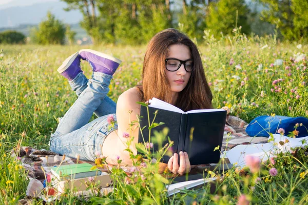Hermosa joven acostada en la hierba y leyendo — Foto de Stock
