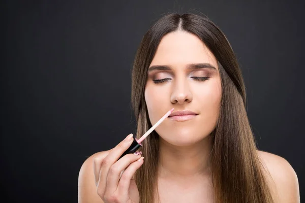 Hermosa mujer joven oliendo el aplicador de brillo de labios — Foto de Stock