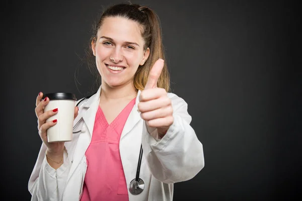 Atraktivní lékařka drží s sebou kávu ukazuje jako — Stock fotografie