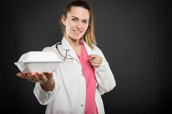 Female young doctor holding and pointing lunch box — Stock Photo, Image