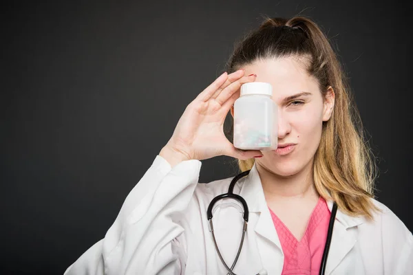 Atractivo médico femenino cubriendo el ojo con una botella de pastillas — Foto de Stock