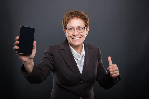 Empresa señora mayor mostrando teléfono inteligente y como gesto —  Fotos de Stock