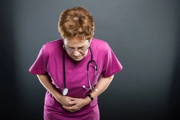 Retrato de una doctora mayor sosteniendo el vientre como lastimada — Foto de Stock