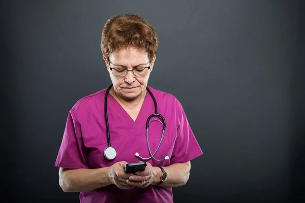 Portrait of senior lady doctor texting on smartphone