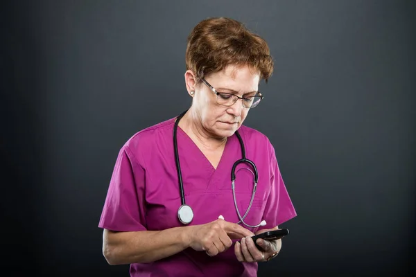 Portrait of senior lady doctor browsing on smartphone