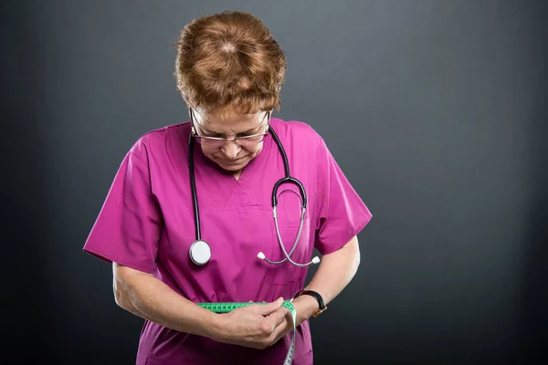 Portrait of senior lady doctor measuring herself with tape