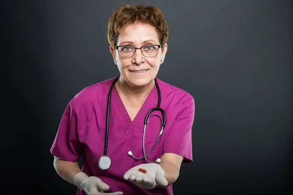 Portrait of senior lady doctor offering one pill
