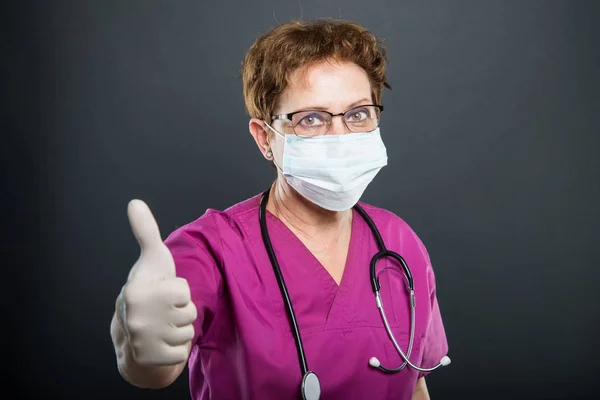 Portrait of senior lady doctor wearing mask showing like — Stock Photo, Image