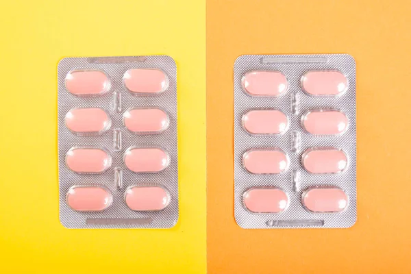 Two blisters of tablets on yellow and orange backgroun — Stock Photo, Image