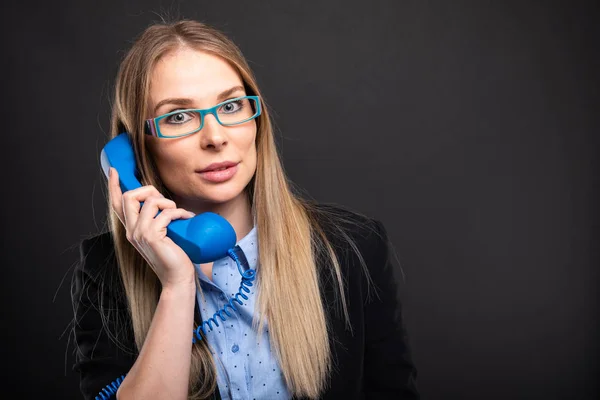 Бізнес-леді в блакитних окулярах розмовляє на синьому отримувачі — стокове фото