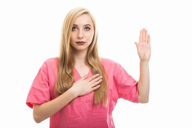 Önlük giymiş genç kadın hemşire portresi beyaz arka planda izole edilmiş bir şekilde yemin ediyor.