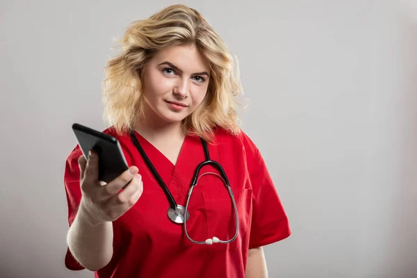 Portrait of nurse wearing red scrub handing smartphone on studio gray background with copy space advertising area