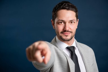 İş portresi genç yakışıklı erkek depolama kravatı mavi arka planda fotokopi alanı reklam alanı ile kamerayı işaret ediyor