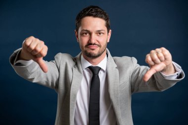 İş portresi. Genç yakışıklı erkek. Mavi arka planda baş parmak hareketini gösteriyor.