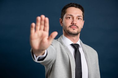 İş portresi genç yakışıklı erkek mavi arka planda fotokopi alanı reklam alanı ile dur hareketi gösteriyor