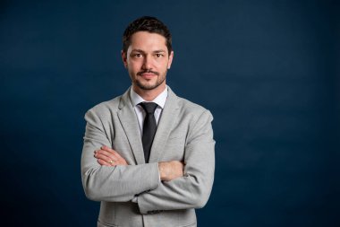 İş portresi. Kolları mavi arka planda ve fotokopi alanı reklam alanında çapraz duran yakışıklı bir erkek.