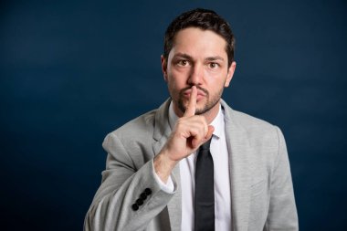 İş adamı yakışıklı erkek, mavi arka planda sessiz jest yapıyor. Fotokopi alanı reklam alanı ile birlikte.