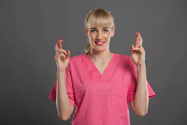 Retrato Jovem Enfermeira Atraente Segurando Dedos Cruzados Fundo Cinza — Fotografia de Stock