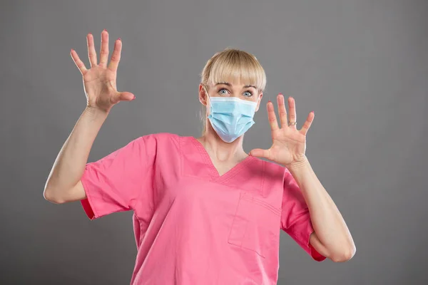 魅力的な女性看護師の肖像顔マスクを身に着けている灰色の背景で怖がっている — ストック写真