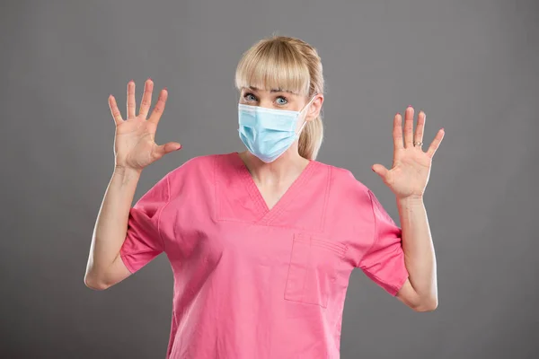 魅力的な女性看護師の肖像顔マスクを身に着けている灰色の背景で怖がっている — ストック写真