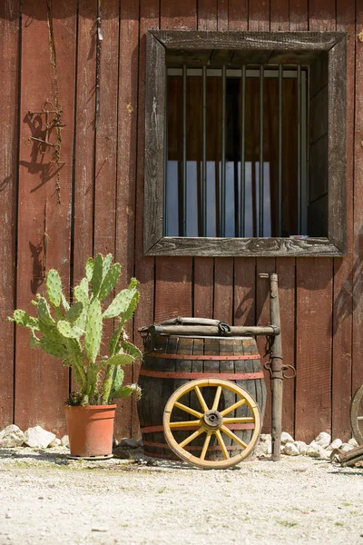 Western style wall, window of hut with barrel, wheel, cactus