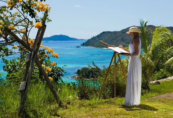 Beautiful, slim woman in white dress paints tropical landscape, sea — Stock Photo, Image