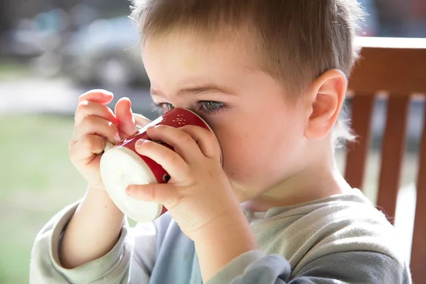 Erkek bebek içecekler, kırmızı-beyaz kupa, açık, doğal ışık — Stok fotoğraf