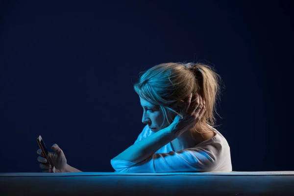 Beautiful blonde woman sits on sofa, and use her cellphone — Stock Photo, Image