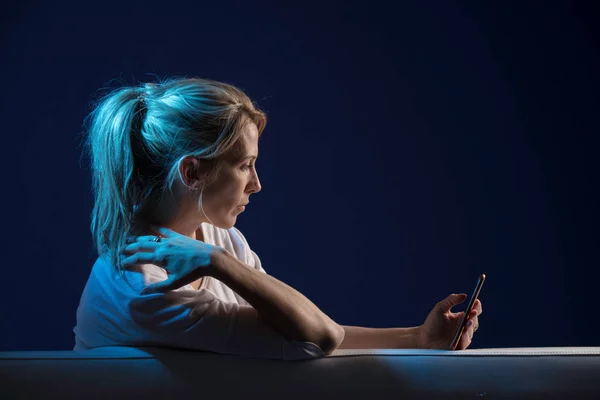 Beautiful blonde woman sits on sofa, and use her cellphone — Stock Photo, Image