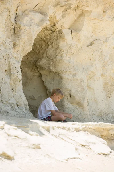 Rapaz loiro solitário senta-se sozinho na entrada de uma pequena caverna — Fotografia de Stock